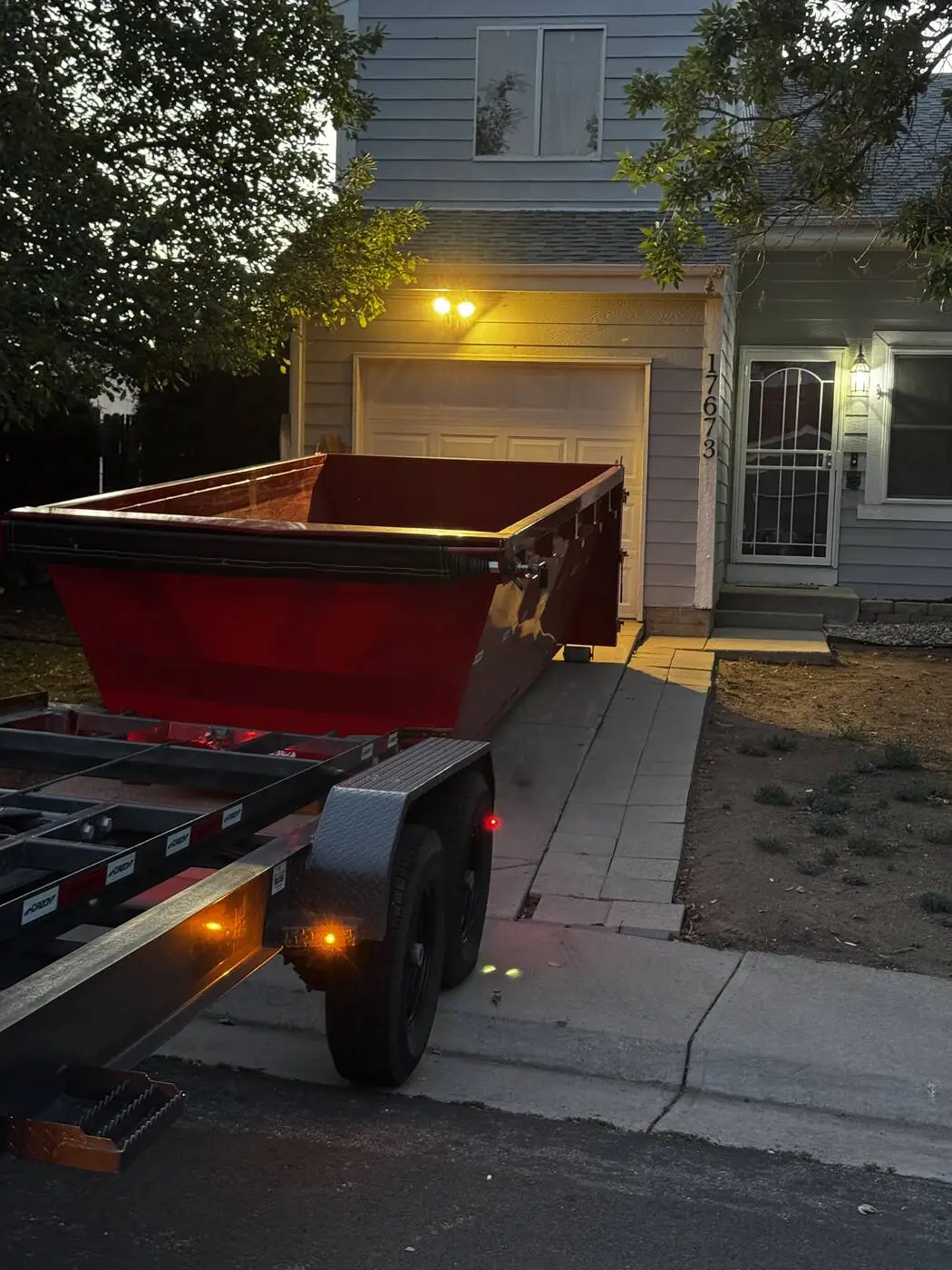 Red roll-off dumpster and trailer in a driveway